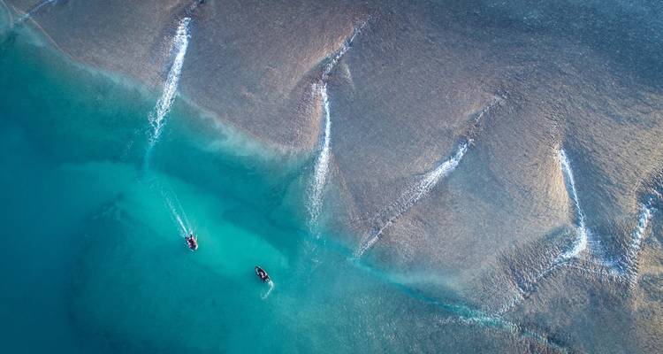 Dramatic aerial of turquoise tidal currents with two speedboats leaving white wakes near Horizontal Falls.