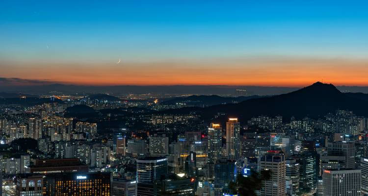Panoramic view of a city skyline at sunset with mountains in the background.