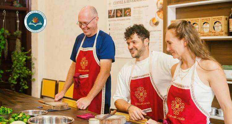 Three people in cooking class setting, wearing aprons and standing at a counter.