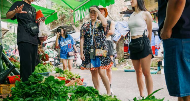Group of tourists at a street market with fresh produce, engaging with a guide.