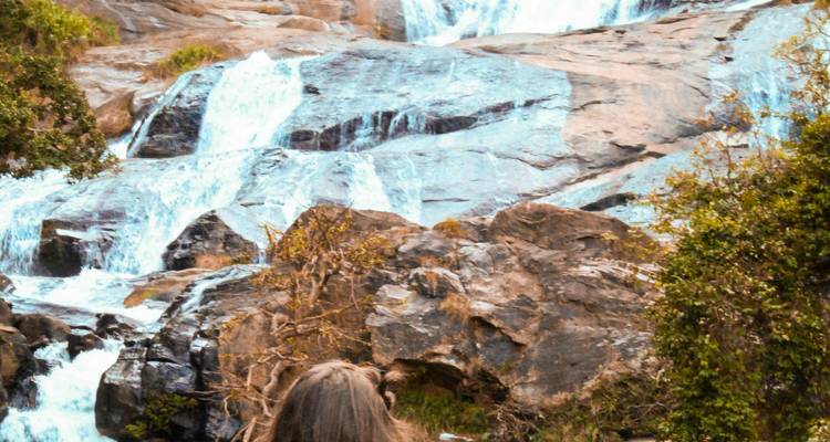 A person viewing a cascading waterfall against rocky terrain.