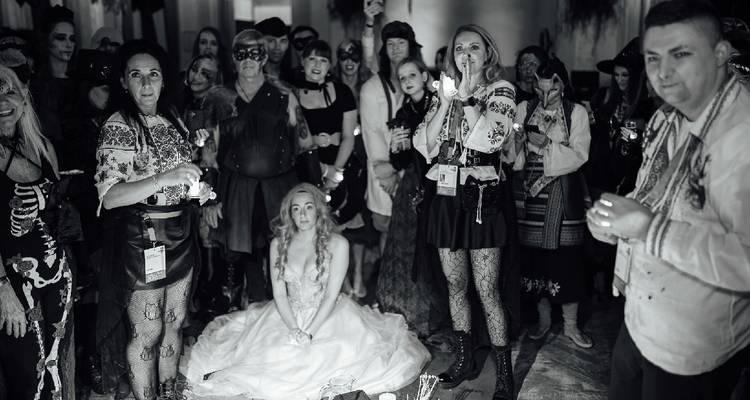 A seated person and others standing in a candle-lit room, dressed in costumes.