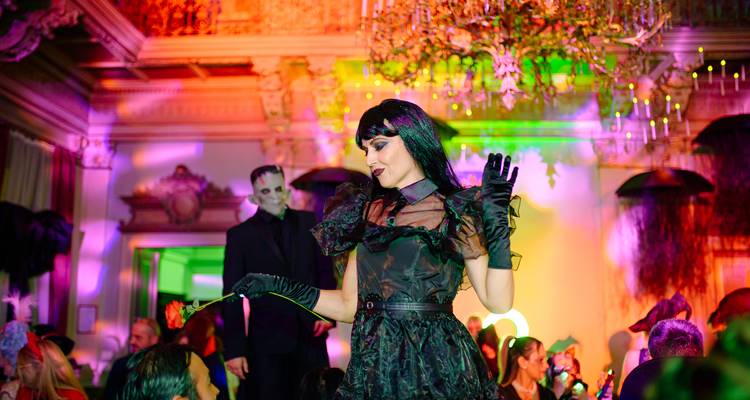 Costumed woman holding a rose on a lit stage with spooky decorations during a Halloween party in Transylvania.