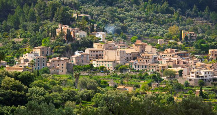 Dorf eingebettet zwischen grünen Hügeln mit sichtbarem Rauch.