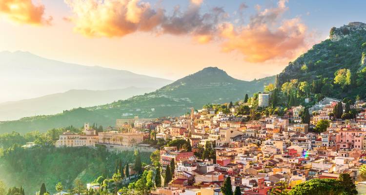 Charming town nestled between mountains, under a sky with clouds lit by sunset.