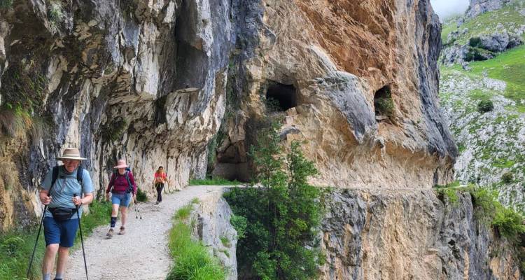 Hikers on narrow Cares Gorge trail carved into limestone cliffs in Picos de Europa.