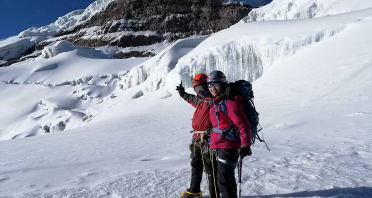 Twee klimmers poseren met ijsbijlen op een breed sneeuwveld met torenhoge ijskliffen op de achtergrond.