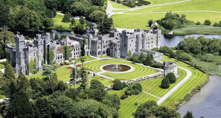 Vista aérea del majestuoso Castillo de Ashford rodeado de jardines cuidados, bosques y un río.
