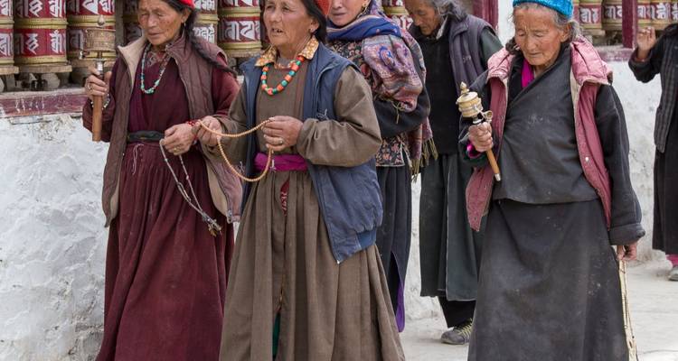 Group of elderly people walking with prayer wheels in a religious setting.