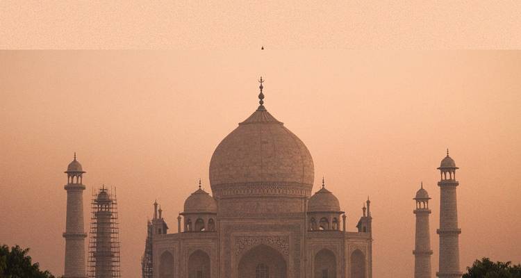 The Taj Mahal under a hazy sky with scaffolding on the minarets.
