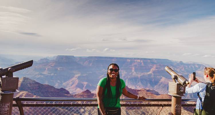 A person smiles at the Grand Canyon's edge with telescopes nearby.