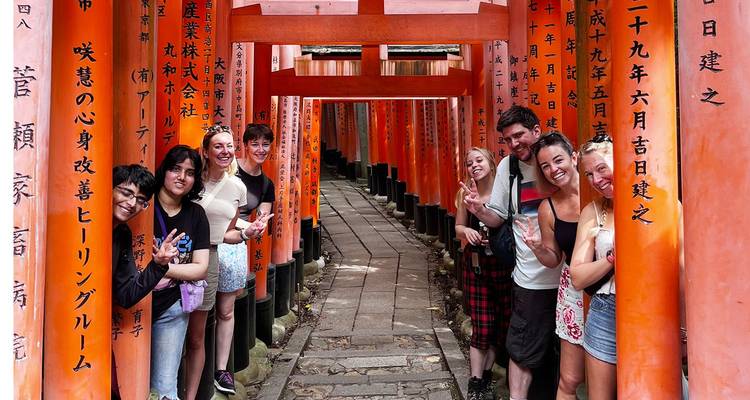 Small tour group posing between vermilion torii gates at Fushimi Inari Shrine in Kyoto.