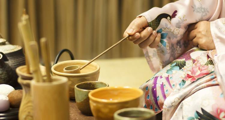 Close-up of a kimono-clad participant preparing bowls during a Japanese tea ceremony.