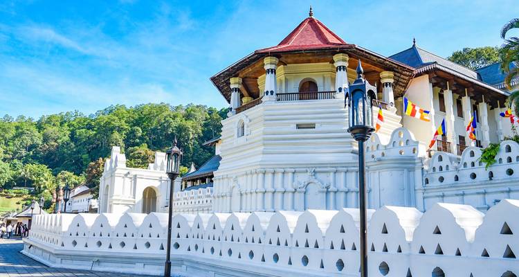 Helle Fassade des Zahntempels von Kandy mit bunten Fahnen unter einem sonnigen Himmel.