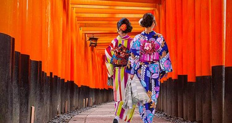 Deux femmes en kimonos marchent dans un corridor de portes torii rouges.