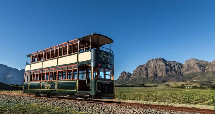 Le tramway viticole à impériale de Franschhoek traverse les vignobles avec les montagnes escarpées du Cap en toile de fond.