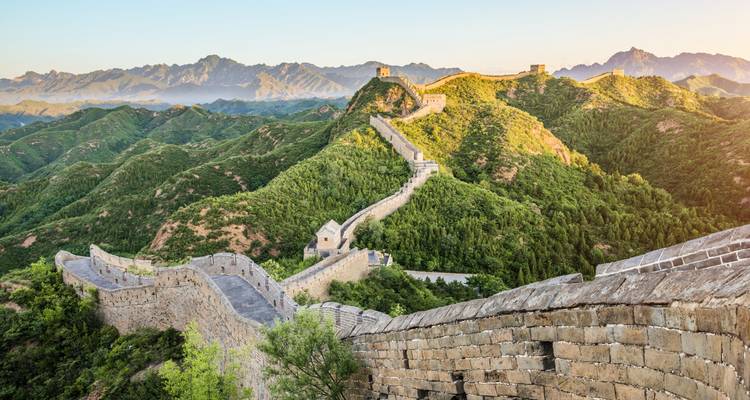 Die Chinesische Mauer schlängelt sich über üppig grüne Berge im warmen Licht der goldenen Stunde.