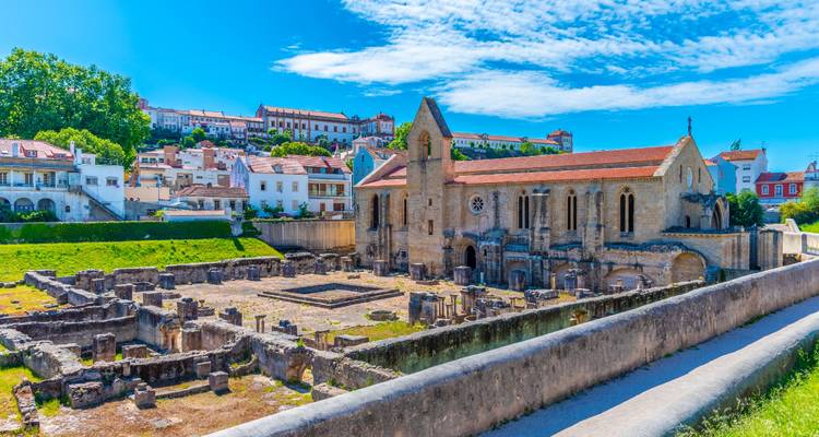 Ruinas históricas de monasterio con paisaje urbano circundante bajo un cielo brillante.