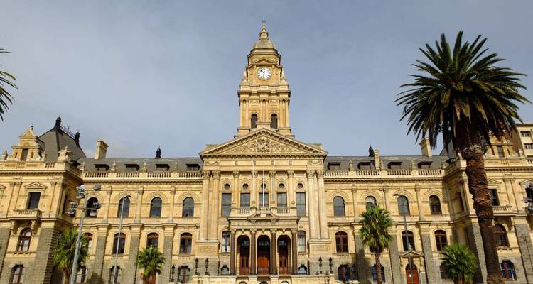 Historic building with clock tower framed by palm trees against a cloudy sky.
