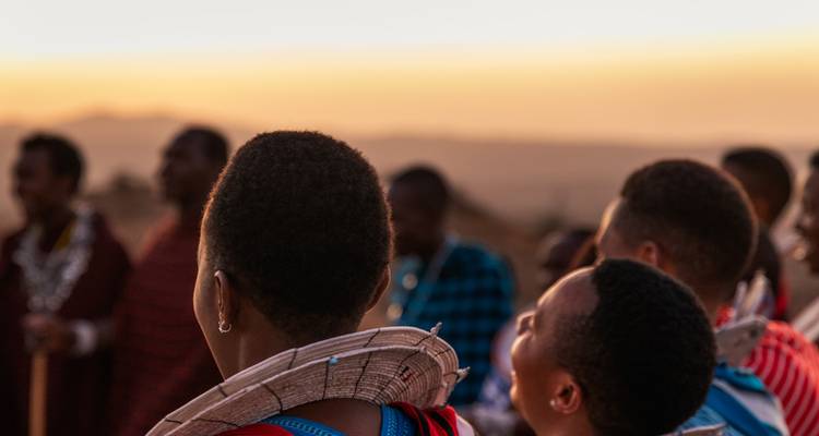 Gruppe von Menschen in traditioneller Kleidung mit einem Sonnenuntergang im Hintergrund.