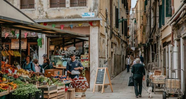 Buitenmarktscène met verse producten en winkelende mensen.