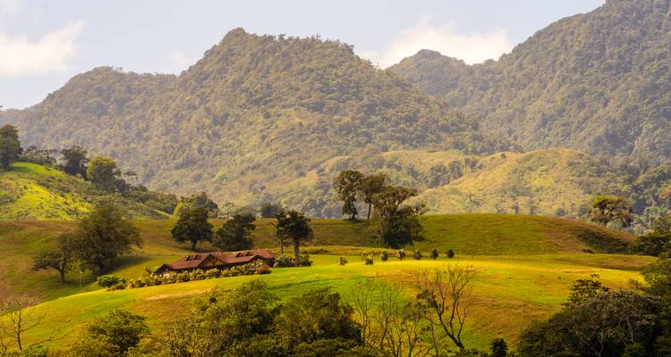 Paisaje rural con una casa rodeada de colinas.