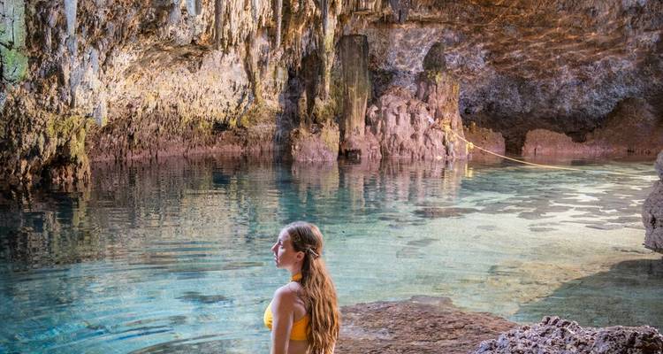 A woman standing in a brightly lit cave with clear water.