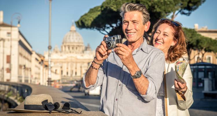 Two people smiling, holding a camera, with St. Peter's Basilica in the background.