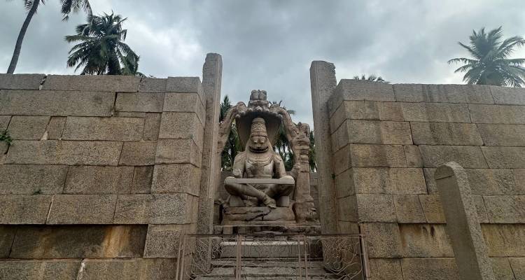 A large stone statue with a backdrop of palm trees and ruins.