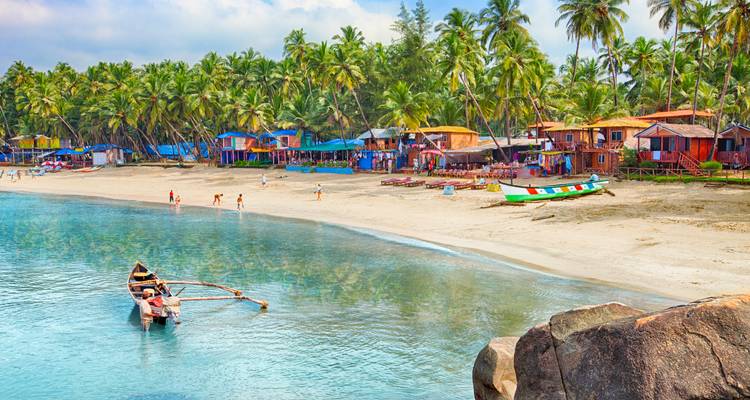 Scenic beach with palm trees and colorful cabins along the shore in Goa, India.