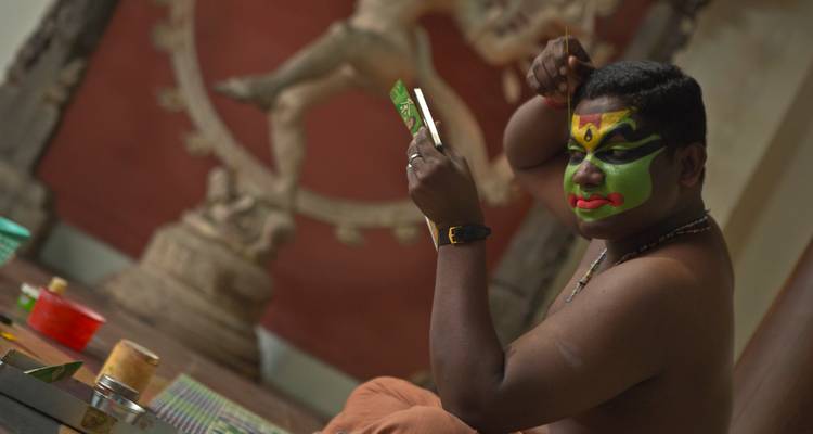 Un artiste applique un maquillage Kathakali vert éclatant en se regardant dans un miroir en coulisses