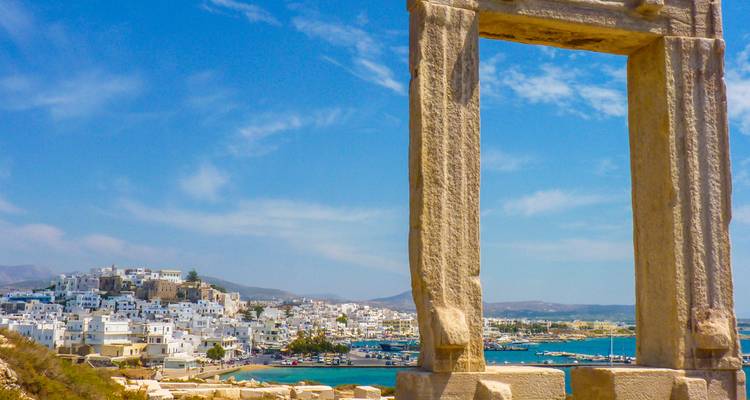 Ruines anciennes surplombant une mer bleue et des bâtiments blancs.