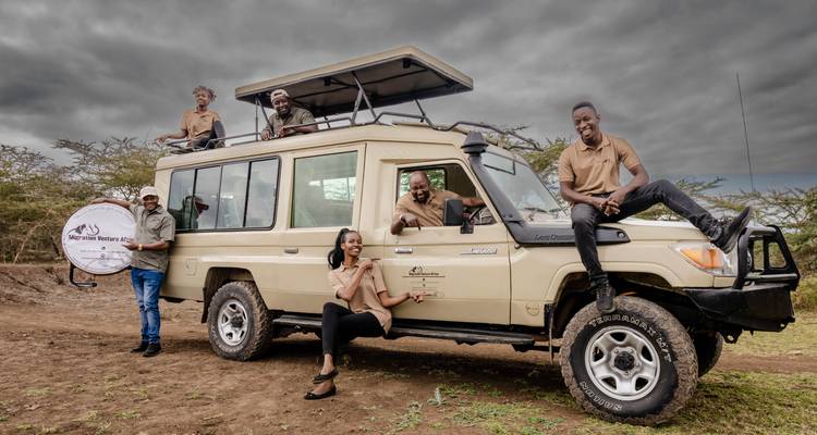 Groupe de personnes posant avec un véhicule de safari dans la savane.