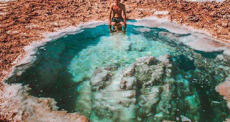 Personne assise près d'un bassin d'eau claire entourée d'un terrain rocheux.