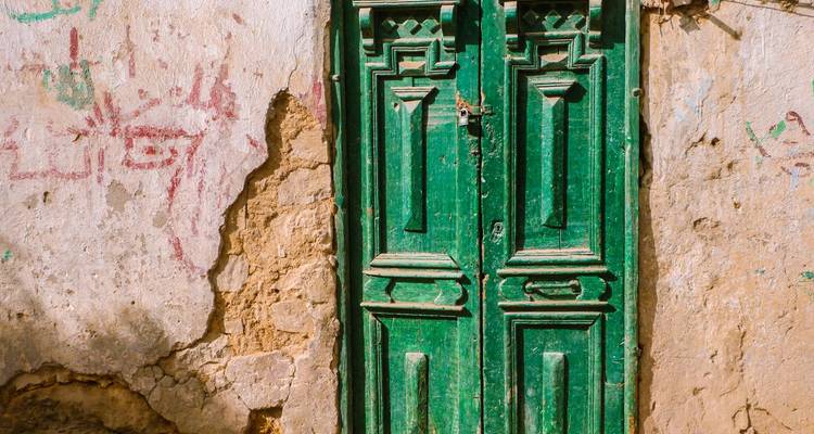 Porte verte sur un mur patiné avec des graffitis.