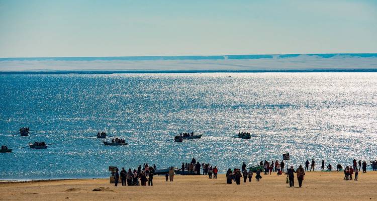 Des gens et des bateaux près d'une grande étendue d'eau sous un soleil éclatant.