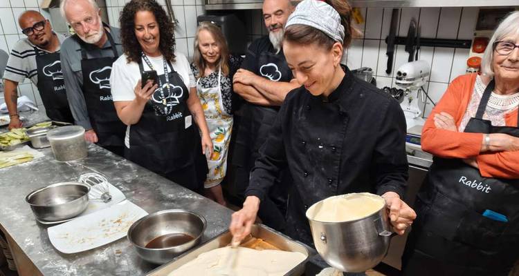 Participants in aprons gather around a chef who spreads creamy dessert filling during a hands-on cooking class.