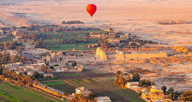 Un globo aerostático rojo solitario se desliza sobre los templos de Luxor y los campos fértiles a la hora dorada.