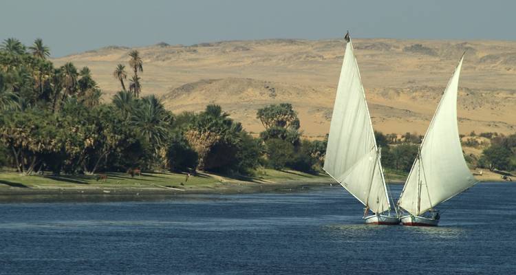 Two traditional feluccas with white sails glide along the Nile against a desert backdrop.