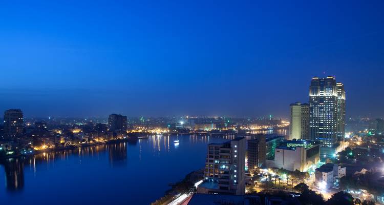 Horizonte de El Cairo por la noche reflejado en el Nilo con edificios de gran altura iluminados y puentes.