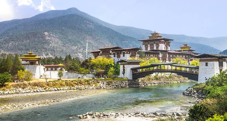 Hermoso dzong construido sobre el río con montañas al fondo.