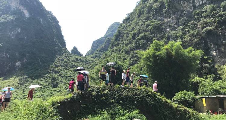 Een groep mensen die op een oude stenen brug staat, omringd door weelderige bergen.