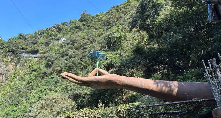 Sculptuur van een grote hand die een plant vasthoudt, omringd door bos.
