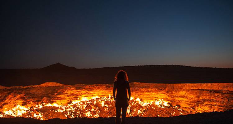 Individual standing before a glowing fire crater at night.