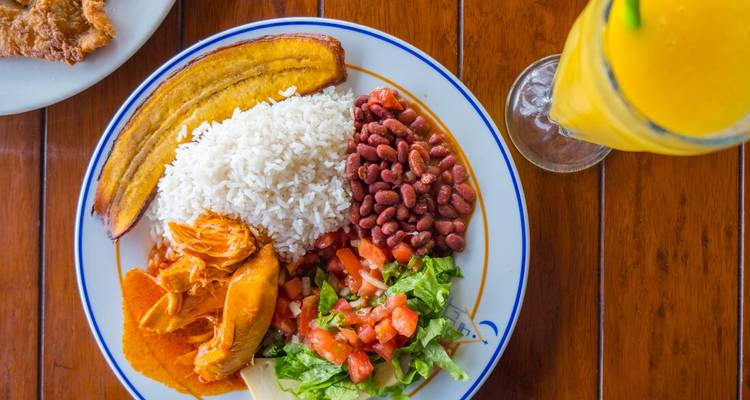 Colorful plate of traditional Costa Rican casado with rice, beans, plantain and chicken beside a tropical juice.