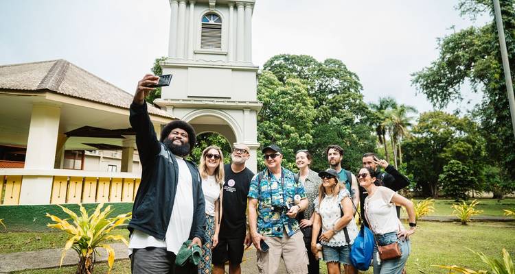 Tourgroep die een vrolijke selfie maakt voor een klokketoren uit het koloniale tijdperk omringd door weelderig groen.