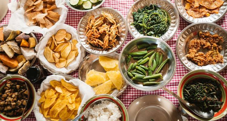 Bovenaanzicht van een kleurrijke Fijische feestmaaltijd met diverse groenten, knollen en tropisch fruit geserveerd op metalen borden.