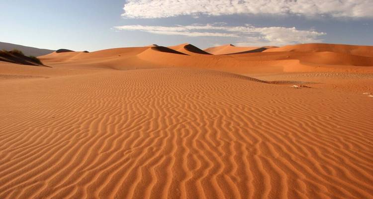 Vue panoramique de dunes de sable avec ciel bleu et nuages.