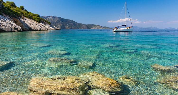 Yacht sur une mer bleue claire près d'un rivage rocheux.