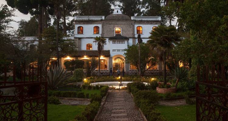 Historical mansion with gardens lit at dusk.